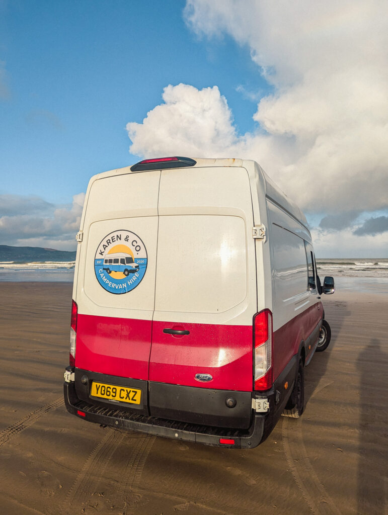 Campervan parked on sandy beach.