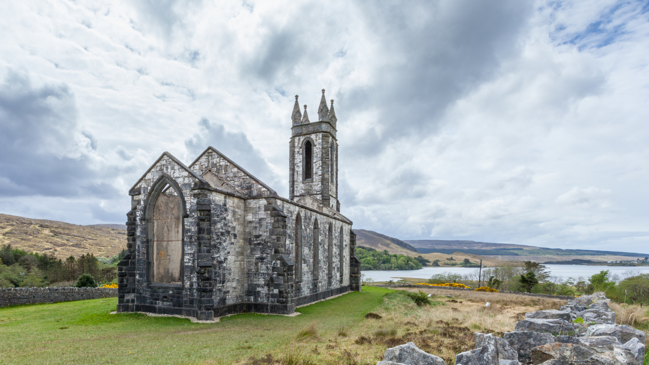 Roofless stone church at Dunlewey with the lough behind it.