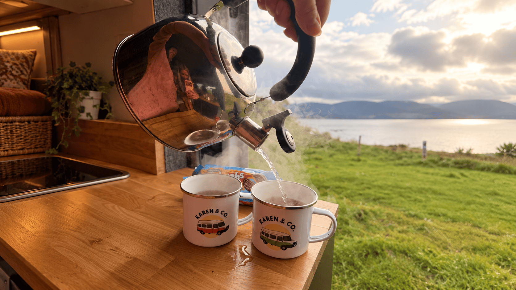 Hot water being poured into two Karen & Co mugs inside a campervan.